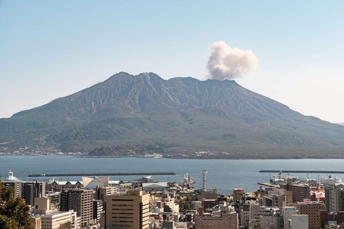 鹿児島市街の向こうにそびえる、噴煙をあげる桜島