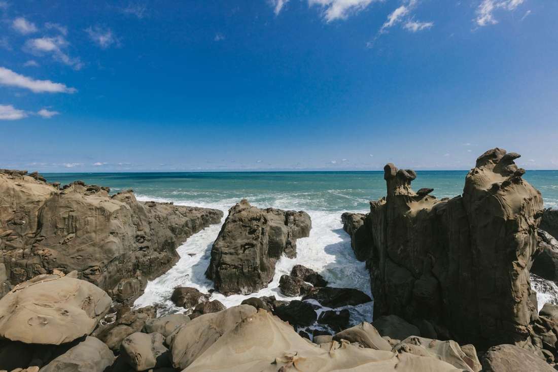 青空の下、波が打ち寄せる岩の海岸